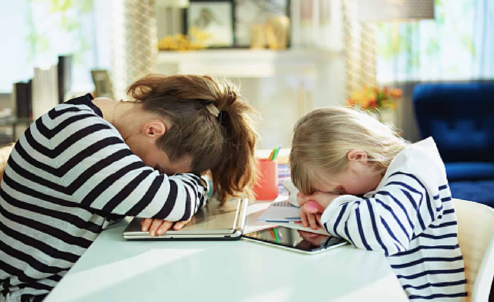 tired young mother and child in striped sweaters in home office in the modern living room in sunny day laying on table